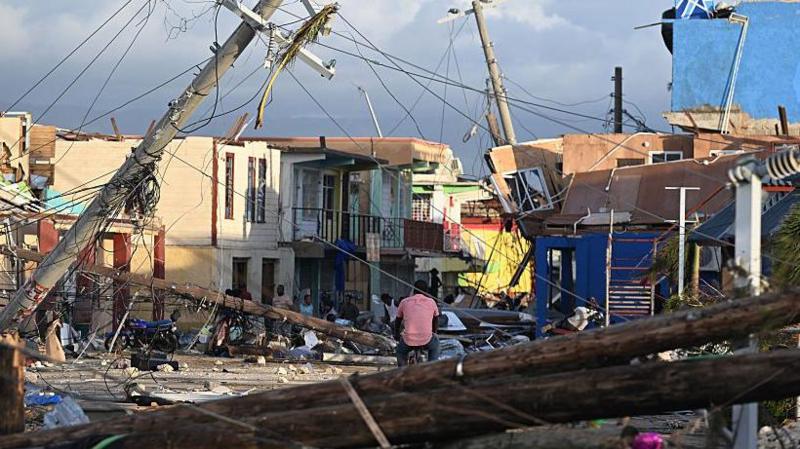 a neighbourhood is destroyed after being hit by a hurricane. Buildings damaged and pylons toppled.